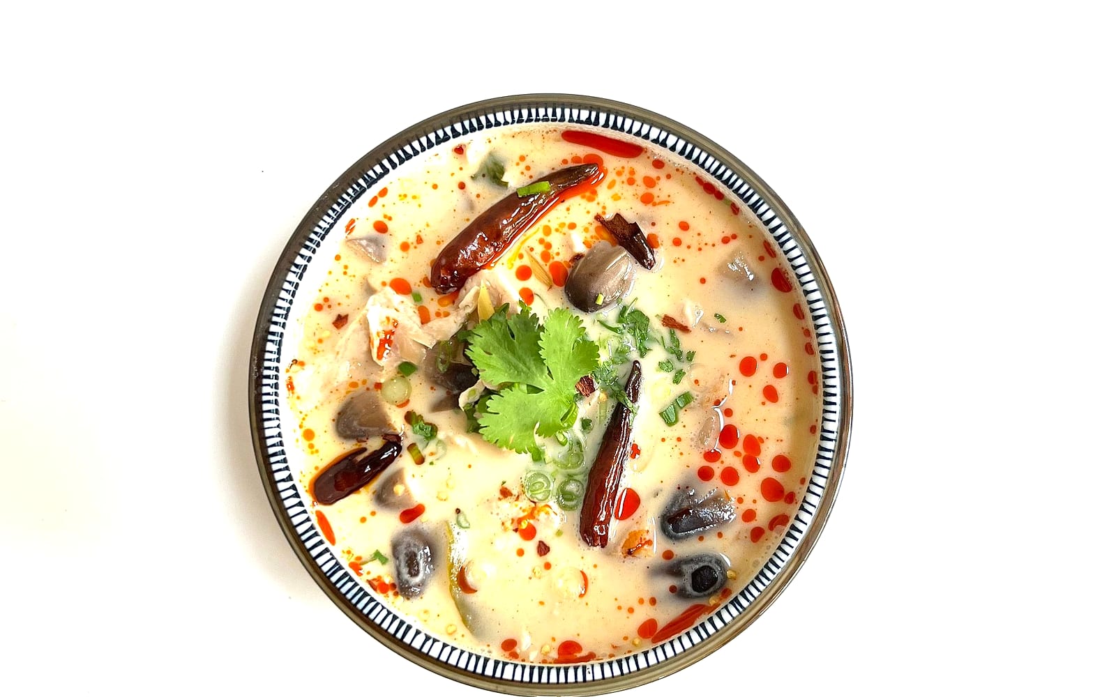 A bowl of creamy coconut soup with dried chilies, mushrooms, cilantro and red chili oil